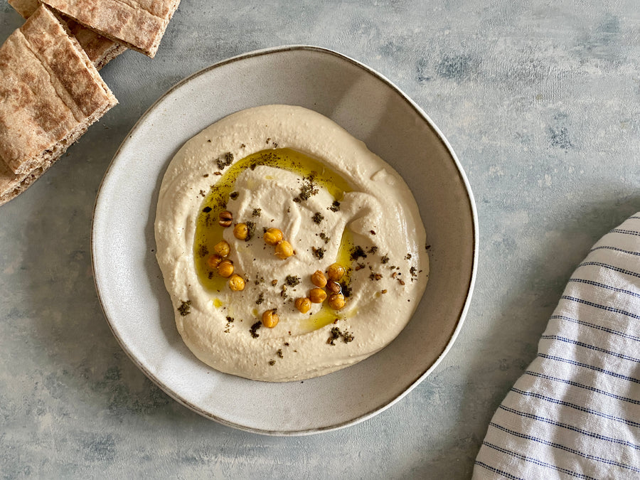 The best hummus recipe, featuring a bowl of homemade creamy hummus made from chickpeas or garbanzo beans and topped with olive oil and pine nuts