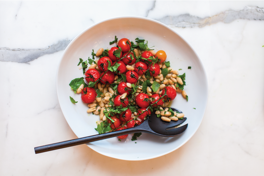 White bowl of white bean with capers, tomatoes and mint.